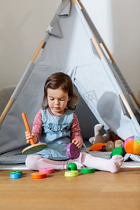 teepee摄影照片_童年，休闲和人的概念—小女婴在家里玩玩具金字塔。快乐的女婴玩玩具金字塔在家里