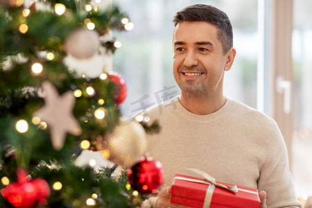 圣诞节，人们和节日的概念-快乐微笑的中年男子在家里拿着礼品盒。快乐的中年男人在家中带着圣诞礼物