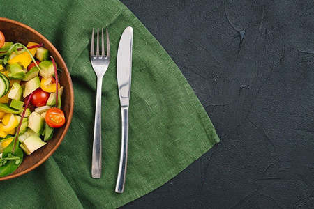 玉米沙拉军舰摄影照片_健康蔬菜沙拉与叉子黄油刀桌布黑色混凝土背景