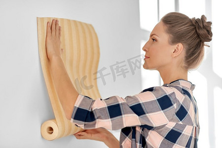 修复，改善和翻新概念—妇女应用壁纸在家里的墙壁。妇女应用壁纸到墙壁在家里