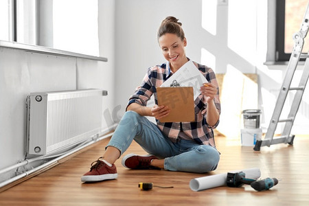 修理，人和房地产概念—妇女与剪贴板坐在地板在家里。妇女与剪贴板坐在地板上在家里