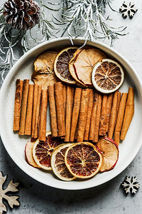 干柑橘切片和肉桂条，放在白色碗里，配上冷杉绿和松果。来自水果和香料的冬季风味。俯视图。