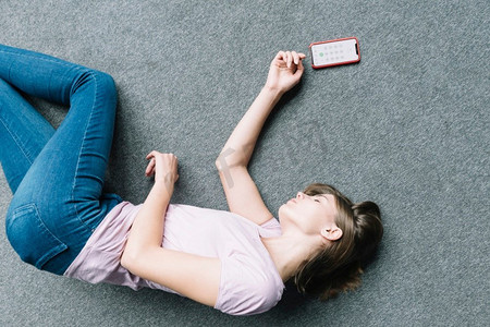 自觉摄影照片_年轻女子不自觉地躺在地毯附近智能手机