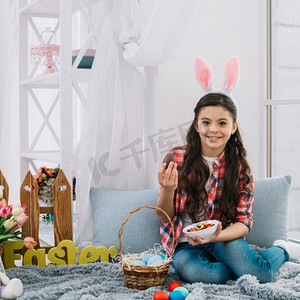 肖像女孩坐在床上举行复活节巧克力鸡蛋碗糖果寻找相机