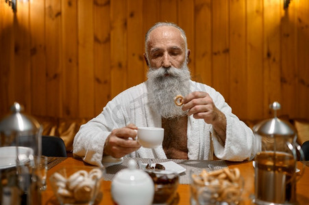 健康程序后，在桑拿浴室休息期间喝茶的灰发胡子高级男子。高级男子喝茶休息在桑拿