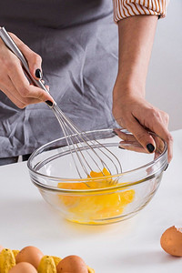 搅拌碗摄影照片_打蛋黄的年轻女子打蛋黄的玻璃碗和打蛋台