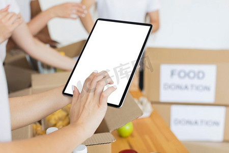 食物捐赠摄影照片_女性志愿者使用平板电脑准备盒子食物捐赠