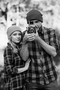 公众号台头摄影照片_河的背景上，一个留着胡子的秃头男人和一个戴着鲜艳帽子的金发女孩正在用一台旧相机拍照