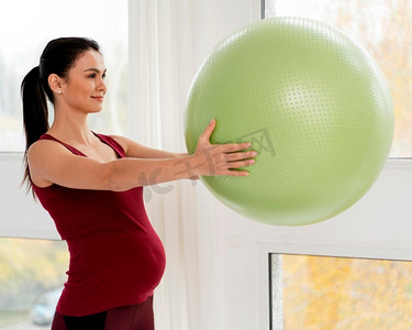 健身球摄影照片_侧着身子的孕妇拿着绿色健身球