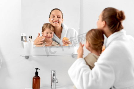 美容、家庭和人的概念-幸福的微笑母女，在浴室里涂上保湿霜。母亲和女儿在浴室里涂了保湿霜
