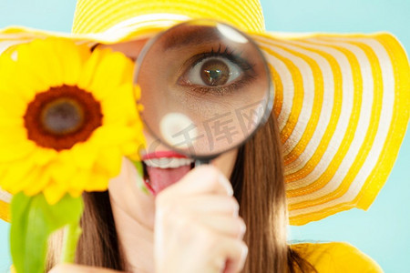 植物学家妇女惊讶的脸表情在黄色帽子审查通过放大镜看花在蓝色背景
