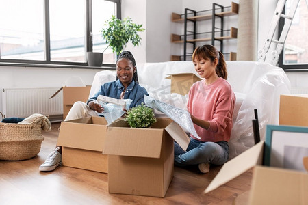 移动，人和房地产概念—快乐的微笑妇女包装或开箱在家里。妇女打开箱子和搬到新家