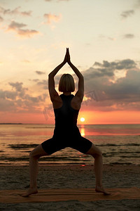 健身、运动和健康的生活方式概念—妇女做瑜伽女神姿势在日落的海滩。妇女做瑜伽女神姿势在海滩