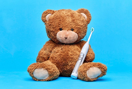 牙齿护理，健康和儿童概念-蓝色背景下带电动牙刷的棕色泰迪熊。带电动牙刷的泰迪熊玩具