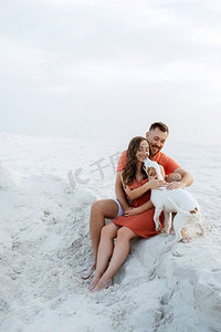 年轻夫妇橙色衣服与狗在沙漠白色的沙滩