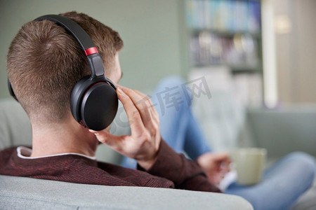 音乐在线摄影照片_男人在家里戴着无线耳机放松在沙发上听流媒体音乐或听播客的特写