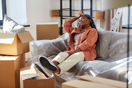 移动，人和房地产概念—疲惫的妇女与盒子休息在沙发在新家。疲惫的女人在搬家时休息