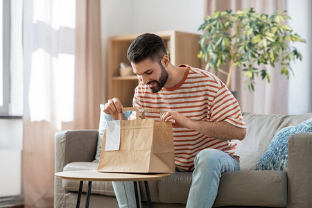 客户家里摄影照片_消费，吃和人的概念—微笑的男人打开外卖食品在纸袋在家里。微笑的男人在家里打开外卖食品