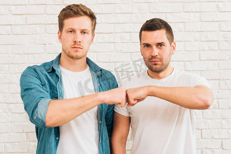 肖像两位男性朋友站在白砖墙上拳头相撞