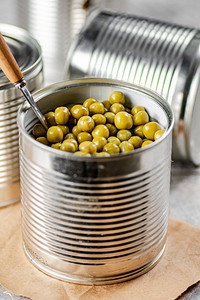 用勺子打开装着青豆罐头的铁罐。在灰色背景上。高质量的照片。用勺子打开装着青豆罐头的铁罐。 
