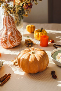南瓜在厨房桌子与自然阳光和阴影，蜡烛和餐具.季节性的秋天静物与橙色装饰。前视图。