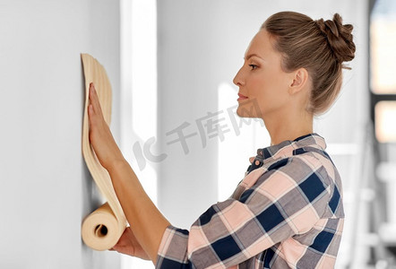 修复，改善和翻新概念—妇女应用壁纸在家里的墙壁。妇女应用壁纸到墙壁在家里