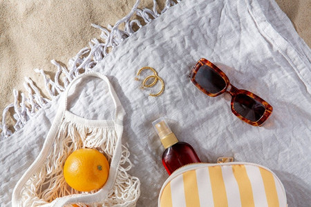 休闲和暑假概念-沙滩毛毯上的橙子和防晒油袋子。沙滩毛毯上的一袋橙子和防晒油