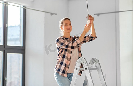 移动，电力和维修概念—妇女更换灯泡在新家。女人在新家里换灯泡
