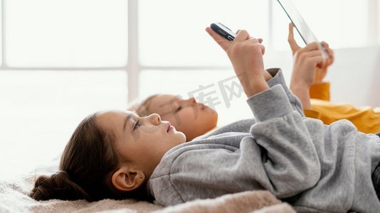 反诈app摄影照片_兄弟姐妹在床上玩手机平板电脑