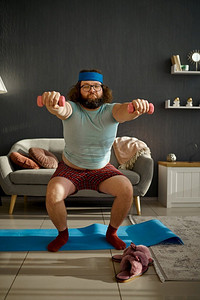 滑稽的胖子在家里背着哑铃晨练。运动、健康的生活方式和减肥。戴着哑铃晨练的滑稽男人