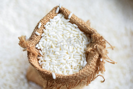 装东西摄影照片_茉莉白米装在袋子里，收获大米放在木桌上，收获大米和粮食做饭的概念