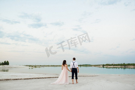 一对年轻的夫妇，一个穿着黑色裤子的男孩和一个穿着粉红色裙子的女孩正沿着沙漠的白色沙滩走着