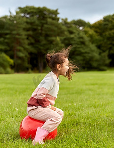 童年，休闲和人的概念—快乐的小女孩跳在公园。快乐的小女孩弹跳在hopper球在公园
