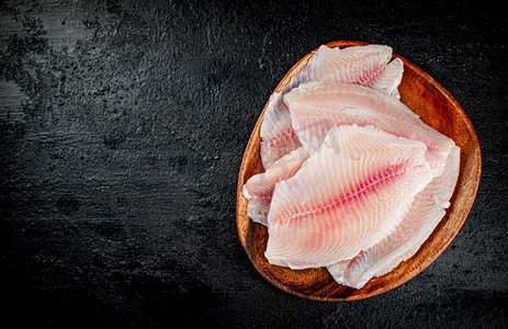 木盘上的新鲜鱼片。在黑色背景上。高质量的照片。木盘上的新鲜鱼片。