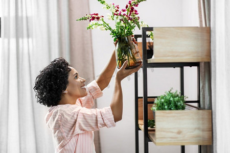 家居装修，装修和人的概念—快乐的微笑妇女放置鲜花货架。妇女把鲜花放在家里的架子上