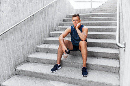 健身，运动和人的概念—疲惫的年轻人与蛋白质摇瓶坐在楼梯。运动员坐在楼梯上瓶子里