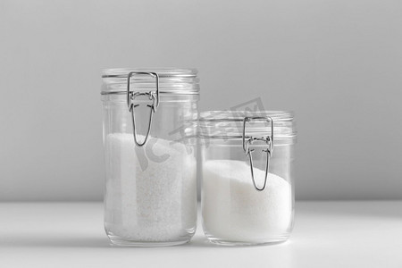 食物，烹饪和不健康的饮食概念—近摄白糖和盐玻璃罐在桌子上。近拍白糖和盐玻璃罐