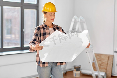 修理，建筑和房地产概念—妇女在头盔与蓝图坐在地板在家里。妇女在头盔与蓝图在家里