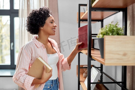 改善摄影照片_家庭改善和人的概念—快乐的微笑的妇女安排书架上的书籍。微笑的妇女安排书籍在书架在家里