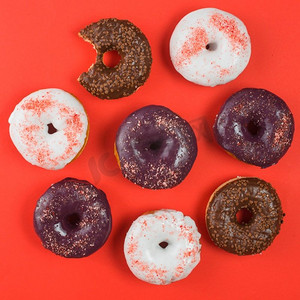 不同的五颜六色的磨砂甜甜圈与咬痕红色背景