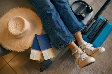 假期旅行行李箱摄影照片_女性腿在行李箱与旅行票作物拍摄。旅途愉快，假期假期。女性腿在行李箱与旅行票