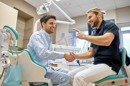 微笑的牙医与男性病人握手。口腔医生给予牙齿治疗和护理建议。微笑的牙医握手与男性患者