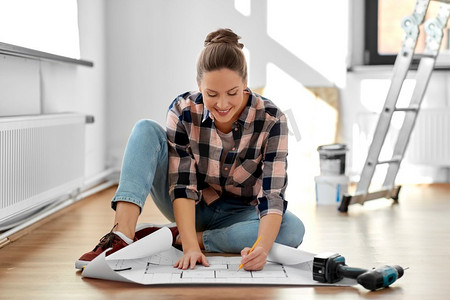 修理，人和房地产概念—妇女与蓝图和铅笔坐在地板在家里。妇女与蓝图坐在地板上在家里