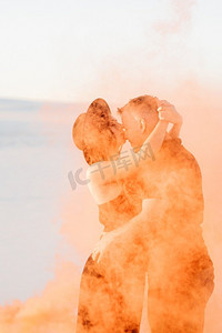 水拥抱摄影照片_男孩和一个女孩在黑色的衣服拥抱和运行在白色的沙滩上与橙色的烟雾