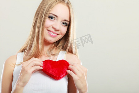 情人节爱情关系还是养生观念。一位年轻的金发女子胸前戴着红心的爱情符号，工作室拍摄于灰色上