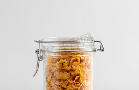储存食品摄影照片_食物储存，吃和储存概念—罐子特写镜头与玉米片在灰色背景。关闭的罐子与玉米片在白色桌子