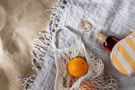 防晒沙滩摄影照片_休闲和暑假概念—一袋橘子和防晒油在沙滩毯子上。一袋橘子和防晒油在沙滩毯子上