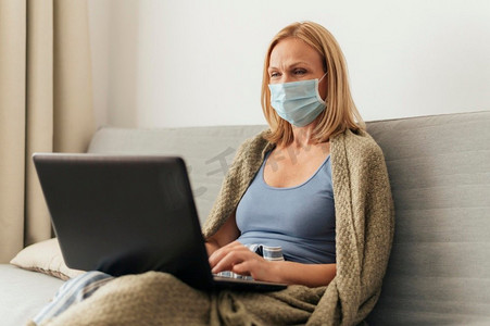 一名妇女在自我隔离期间带医用口罩在家工作笔记本电脑