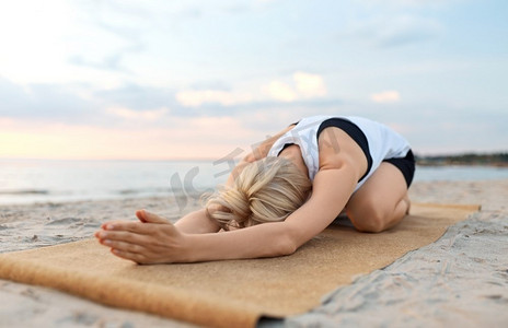 健身，运动，和健康的生活方式概念—妇女做瑜伽儿童姿势在海滩超过日落。妇女做瑜伽儿童姿势在海滩