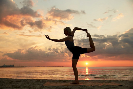 健身、运动和健康的生活方式理念--日落后在海滩上做瑜伽舞者的姿势。日落后，一名女子在海滩上摆瑜伽舞姿势